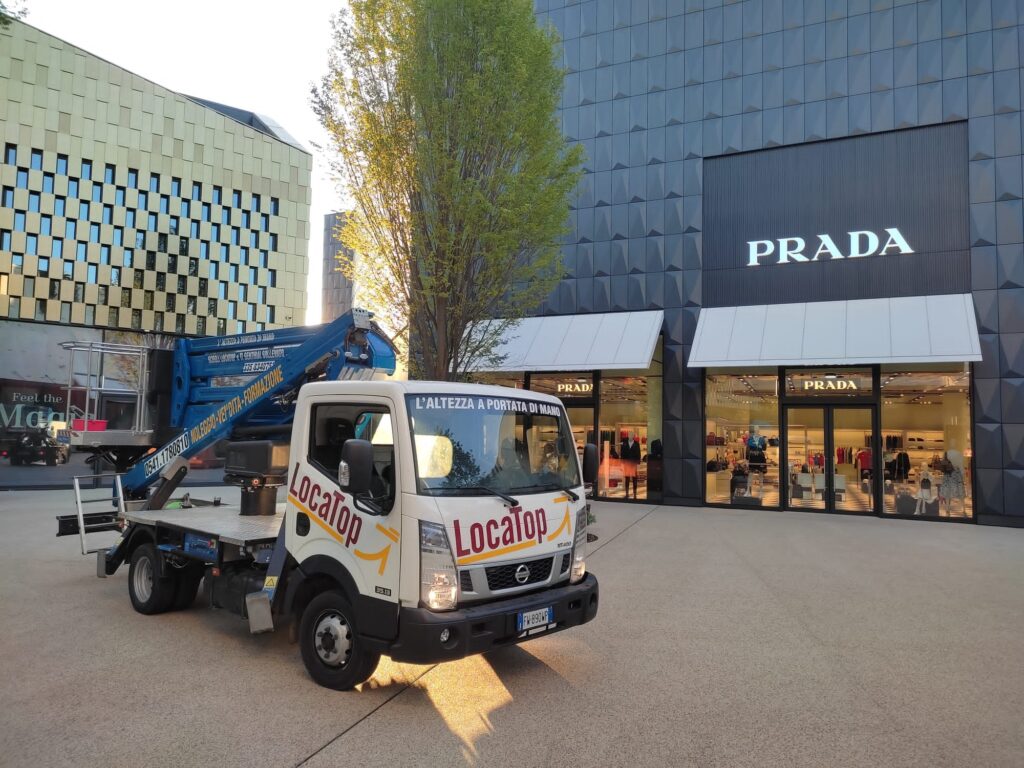 Piattaforma aerea per manutenzione in centri commerciali, mezzo Loca Top davanti a negozio Prada in galleria retail